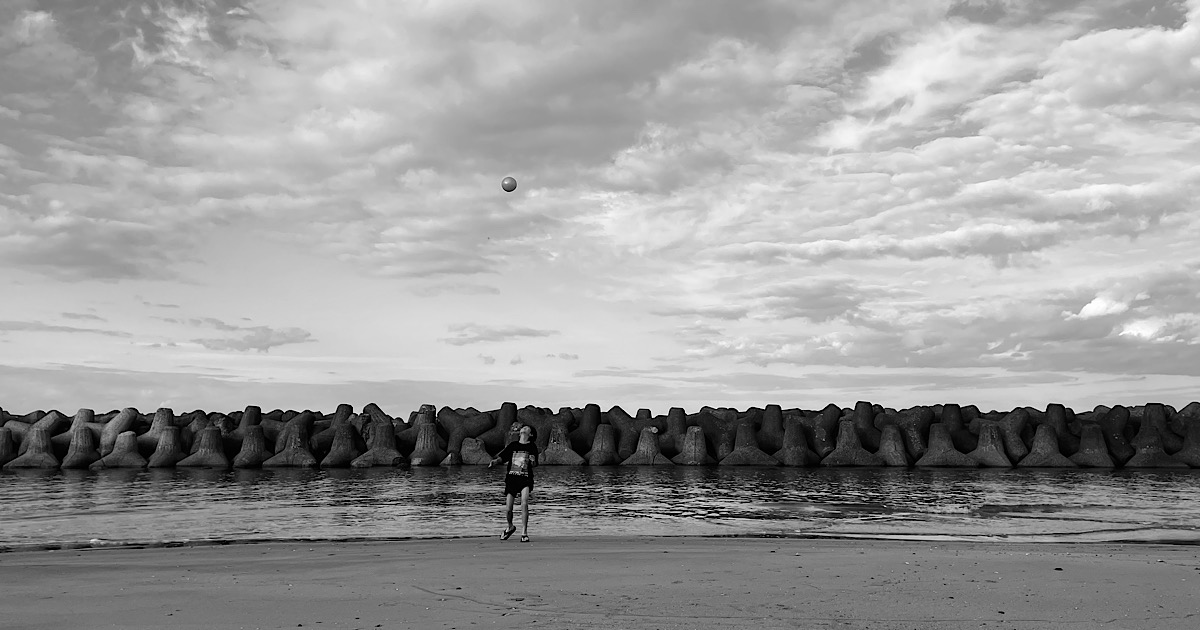 海岸で高く上げたボールを見つめる少年