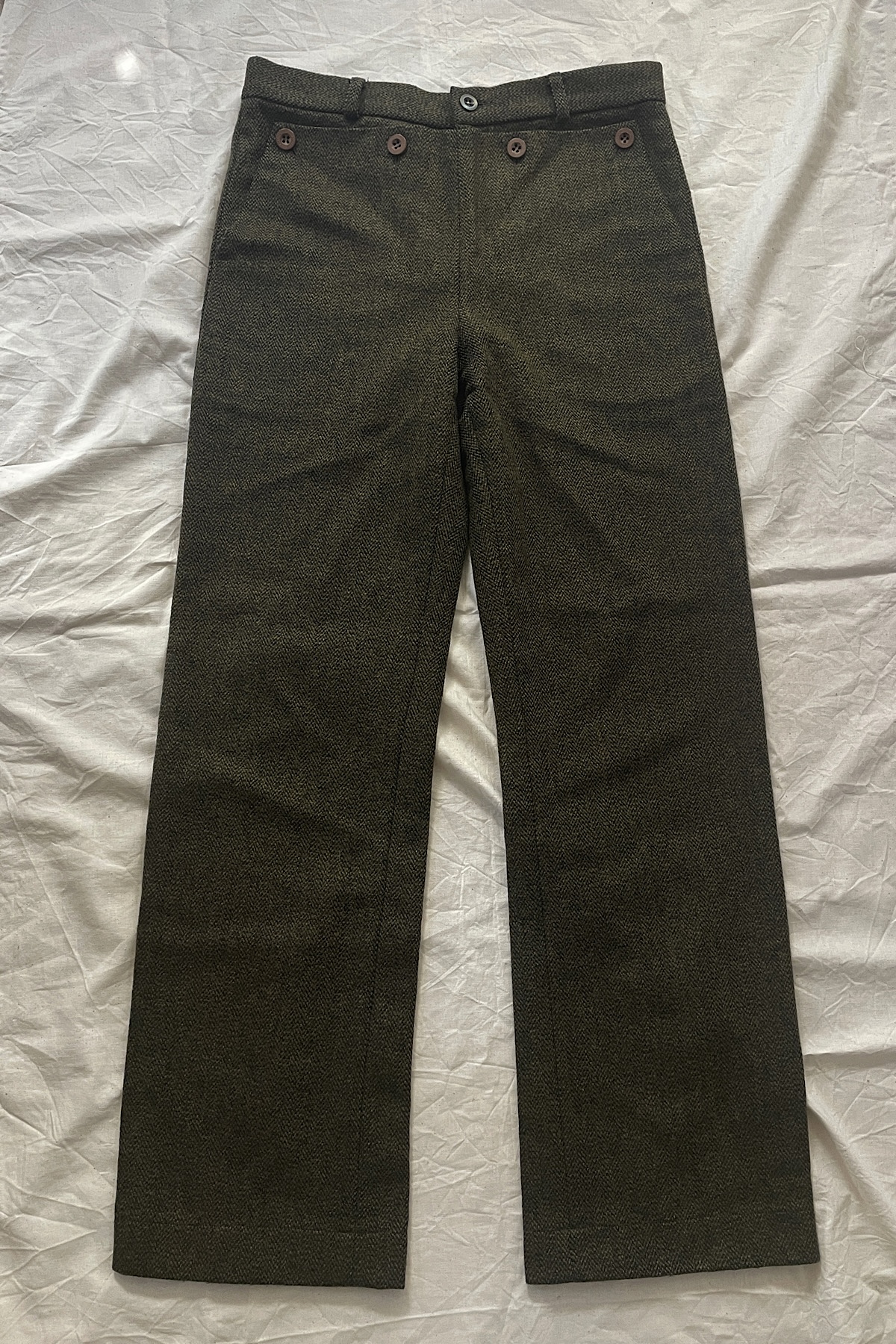 深緑のパンツが生成りの布の上に置かれた様子