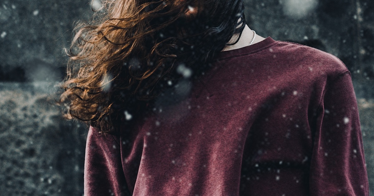 雪がチラつく中で立ち尽くす髪の長い男性