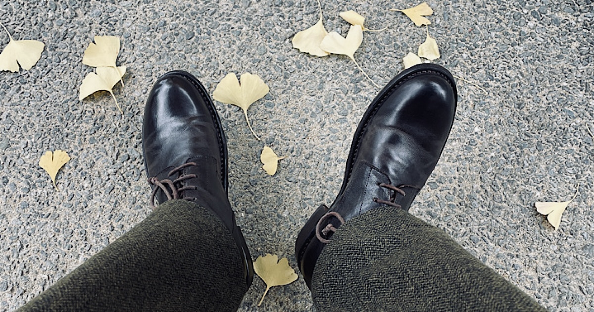 落ち葉の落ちたアスファルトと革靴を撮影した様子